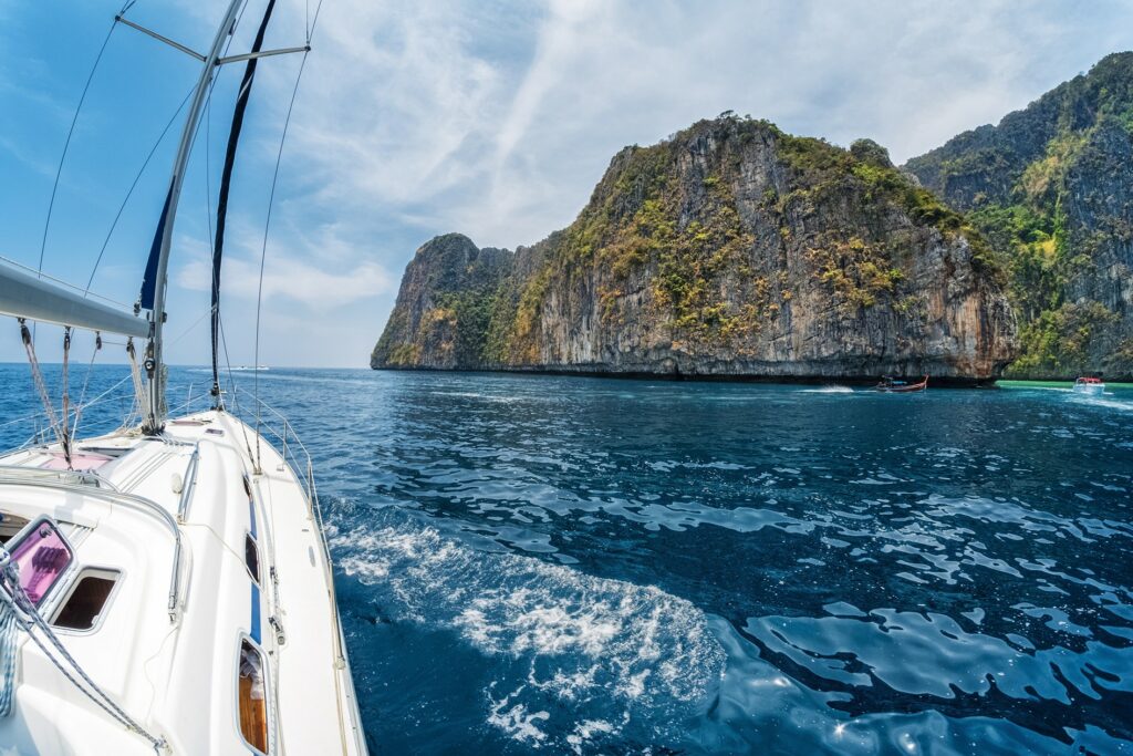 Sailing yacht passing by a rocky cliff on its route